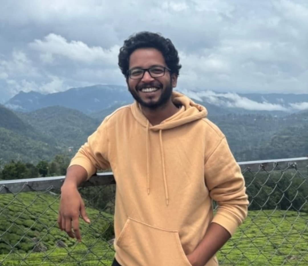 Adithya Reddy, a growth marketer from Hyderabad, smiling in a tan hoodie with green hills behind him